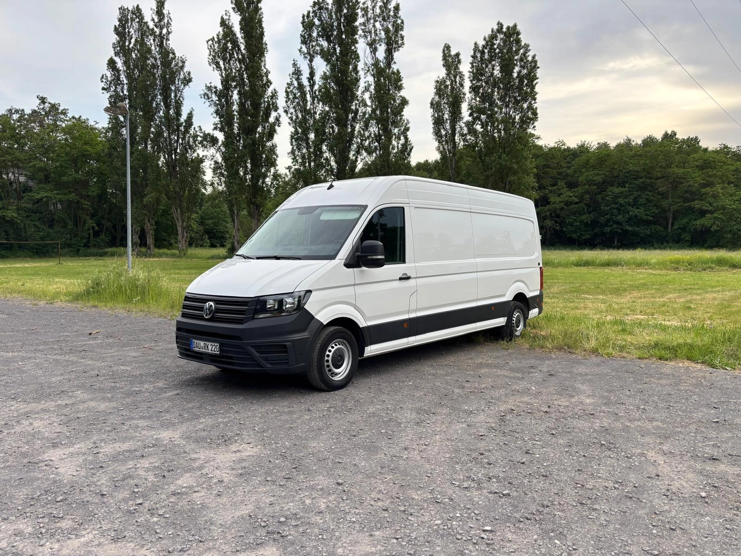 RK-TRANSPORTE – Transport- und Logistikdienstleistungen – Weißer Volkswagen Lieferwagen, geparkt auf Schotter neben einer Wiese.